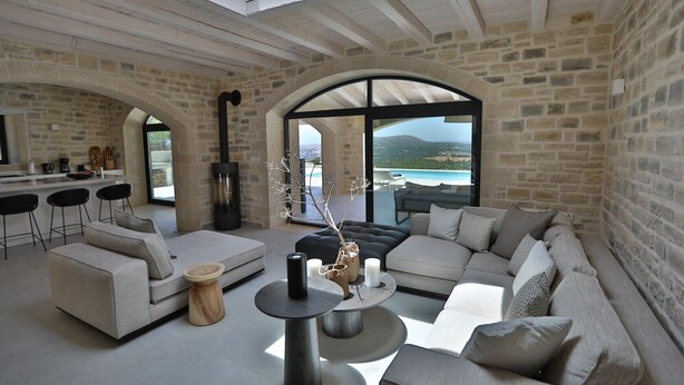 Un salón espacioso con una pared de piedra, un sofá grande, una mesa de centro y vistas al mar.