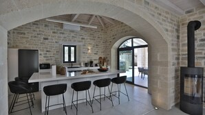 Una cocina moderna con una pared de piedra, un ventanal grande, una estufa empotrada y taburetes de bar.