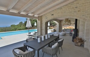 An outdoor patio with a pool, stone walls, wicker furniture, and a TV. - new natural stone villa with large pool and great sea views (Prines)