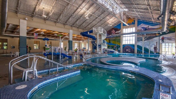 An indoor swimming pool with multiple lanes, a water slide, and a mural on the ceiling.