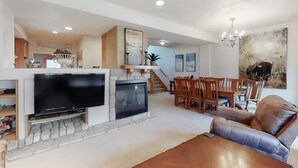 A living room with a fireplace, a television, a dining area with wooden chairs, and a large painting on the wall.