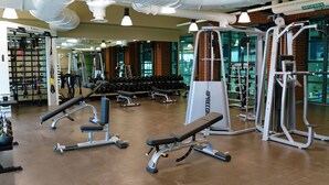 A gym with various exercise equipment, including benches and weight machines, and a rack of dumbbells.