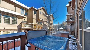 A hot tub on a balcony with snow on the ground and surrounding buildings.