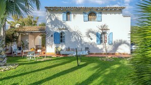 A white building with blue shutters, a patio with chairs and a table, and a hammock. - Villa 'Casa Vacanza Cristina' with Private Pool, Terrace, and Wi-Fi (Plemmirio)