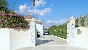 A gated entrance with a white wall and a palm tree. - Villa 'Casa Vacanza Cristina' with Private Pool, Terrace, and Wi-Fi (Plemmirio)