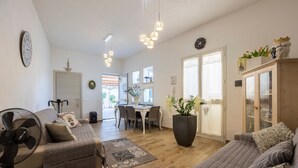Ein Wohnzimmer mit Sofa, Ventilator, Couchtisch, Essbereich mit Tisch und Stühlen sowie einer großen Küsterpflanze.