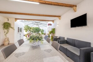 A dining area with a long table, wicker furniture, and hanging plants.