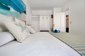 Une chambre à coucher avec un lit, un tableau représentant des vagues, une armoire et une porte donnant sur une autre pièce.