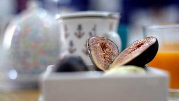 A close-up of a half-cut fig on a white object, with a glass of orange juice and a decorative container in the background.