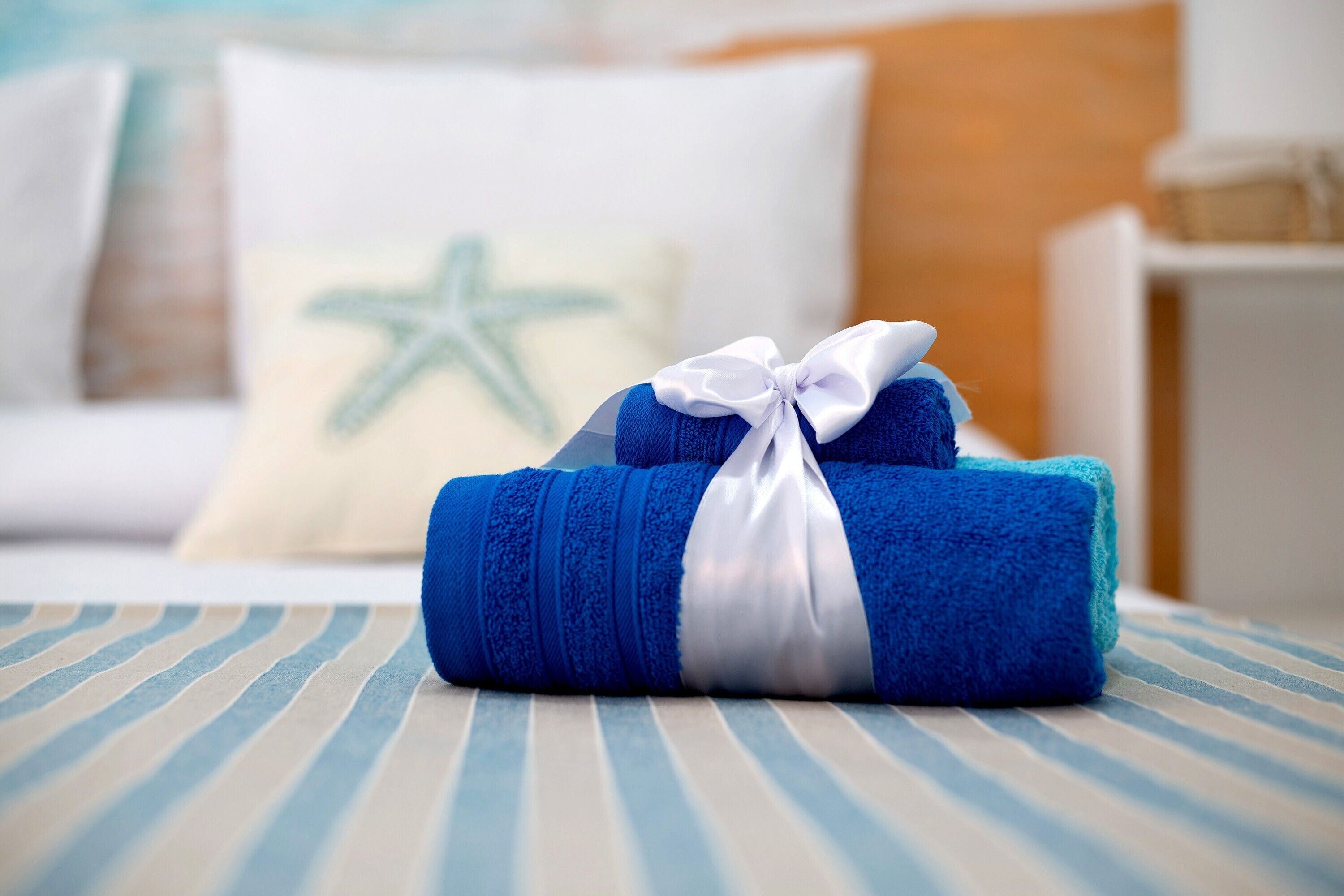 Een keurig opgevouwen blauwe handdoek met een witte strik op een gestreepte spreidekker.