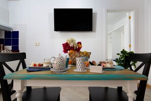Une table à manger recouverte d’une nappe turquoise, un téléviseur fixé au mur, ainsi qu’une variété de vaisselle et d’objets de décoration.