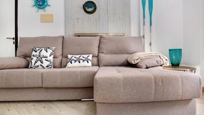 A beige sectional sofa with starfish pillows, a wooden wall with a ship's wheel decoration, and two blue paddles leaning against the wall. - Vacation Home 'Holidays Maxorata Relax' close to the Beach with Wi-Fi (Gran Tarajal)