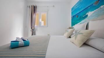 Una camera d'albergo con un letto, una finestra con tende e un quadro che raffigura l'oceano, con un asciugamano sul letto.