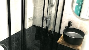 A shower enclosure with a glass door, a sink with a black basin, and a mirror above the sink.