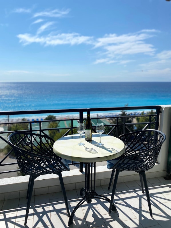 A round table with two chairs, a bottle of wine, and two glasses on a balcony overlooking the sea.