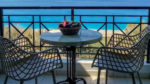 A balcony with a table and chairs, a basket of fruit, and a view of the sea.