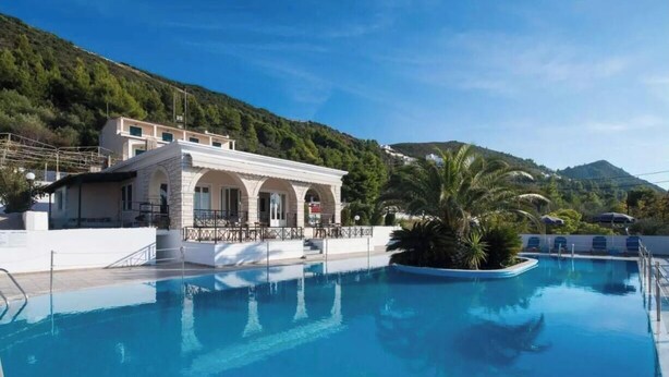 A swimming pool with a building in the background, surrounded by greenery and hills. - Apartment in a Hotel 'Sunset Premium Studio 1' with Sea View, Shared Pool, & Wi-Fi (Lefkada)