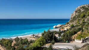 A coastal view with a beach, a restaurant, and a rocky hillside. - Apartment in a Hotel 'Sunset Premium Studio 1' with Sea View, Shared Pool, & Wi-Fi (Lefkada)