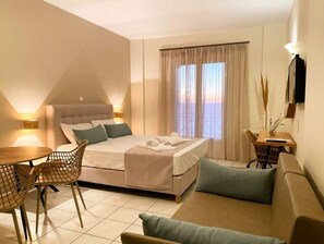 A modern hotel room with a bed, a dining table, and a sofa.