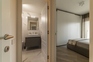 A bedroom with a bed, a bathroom with a sink and mirror, and a door leading to another room. - GuestHost - Modern Apartment with a Terrace in Trastevere (Roma)