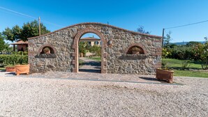 Un arc en pierre mène à un bâtiment dont le toit est recouvert de tuiles, et qui est entouré de gravier et de plantes en pot.