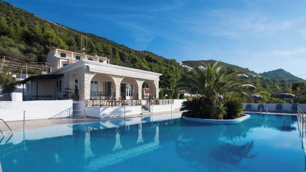 A swimming pool with a building in the background, surrounded by greenery and hills. - Apartment in a Hotel 'Sunset Premium Studio 9' with Sea View, Shared Pool, & Wi-Fi (Lefkada)
