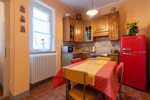 Een keuken met houten kastjes, een rode koelkast, een eettafel met een gele tafelkleed en een raam met gordijn.