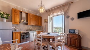 Una cocina con armarios de madera, una mesa de comedor con sillas, una lámpara de araña y un televisor en la pared.
