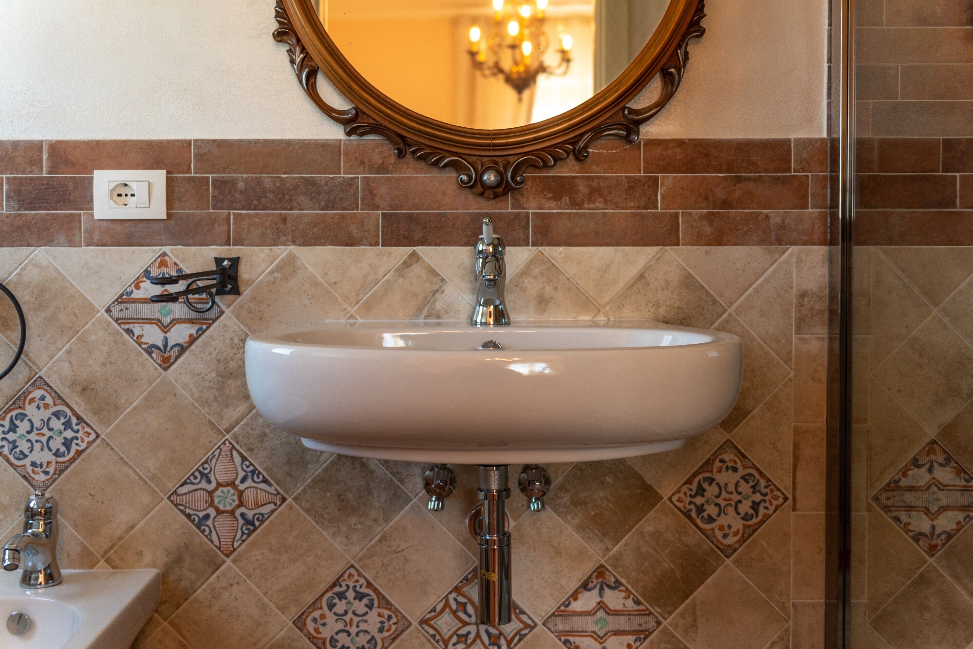 A bathroom with a white sink, a mirror, and patterned tiles.