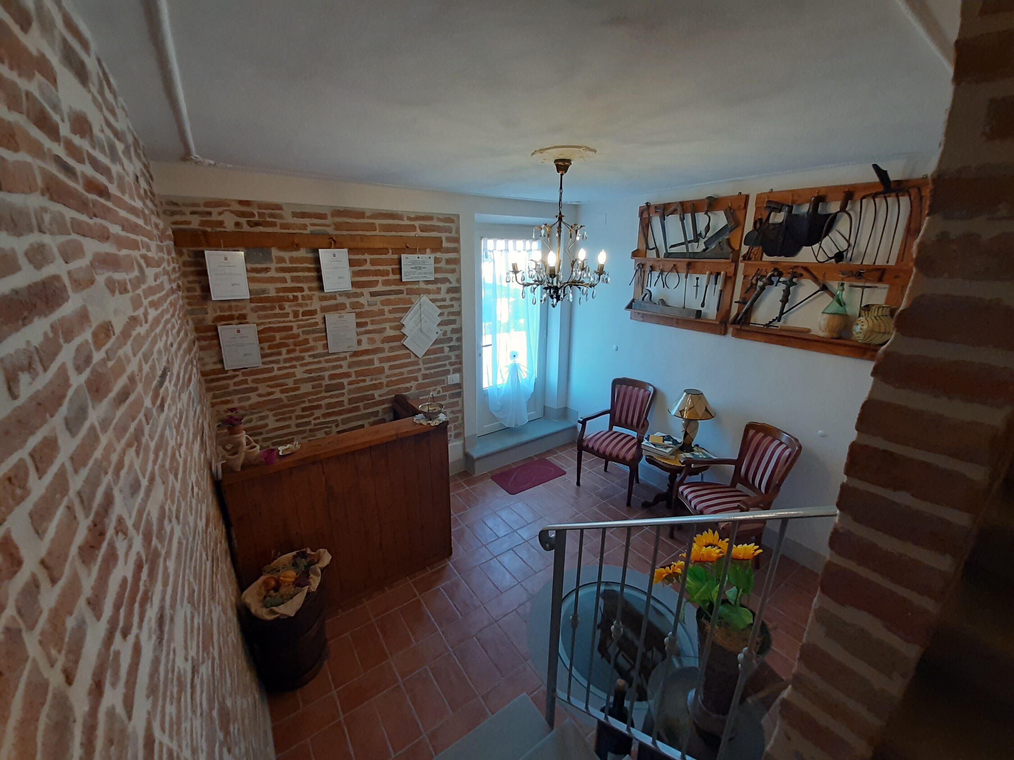 Amplia sala de estar con pared de ladrillo, mostrador de recepción de madera, candelabro y escalera con barandilla.