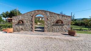 Un arco de piedra que da paso a un edificio con techo de tejas, rodeado de grava y plantas en macetas.