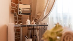Un baño con pared de ladrillo, un espejo, un perchero, un lavabo y un florero con flores.