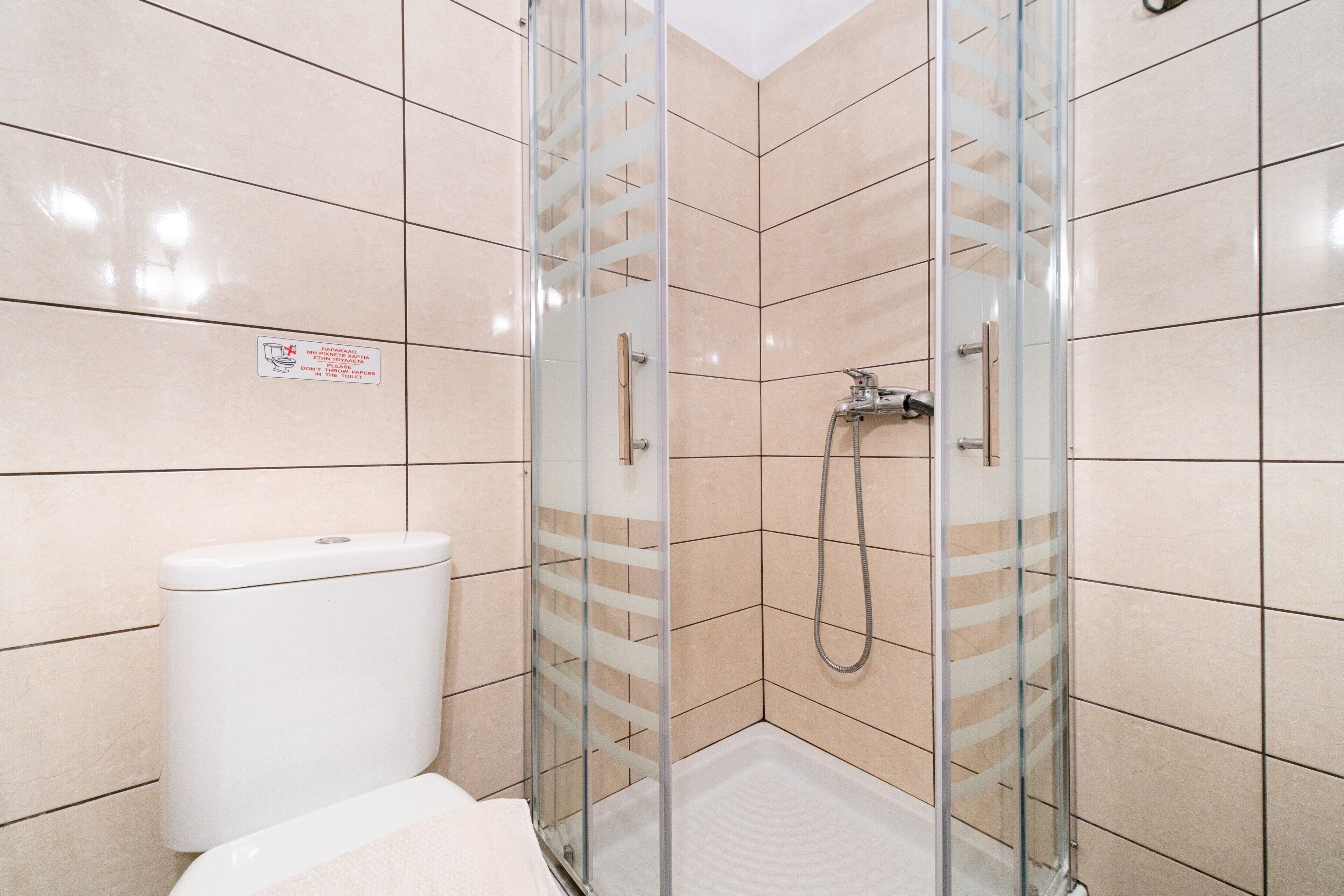 Een badkamer met een douchecabine van glas, een toilet en betegelde wanden.