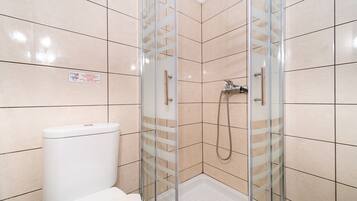 Een badkamer met een douchecabine van glas, een toilet en betegelde wanden.