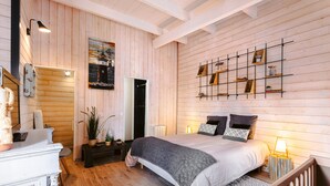 A bedroom with wooden walls, a bed with pillows, a bedside table, a wall-mounted shelf, and a hanging light fixture. - 'Villa la Forge Expérience Bien-Être' with Pool & Wi-Fi (Nuaillé-d'Aunis)