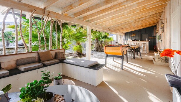 A covered outdoor seating area with wooden beams, a sofa, and potted plants. - 'Villa la Forge Expérience Bien-Être' with Pool & Wi-Fi (Nuaillé-d'Aunis)
