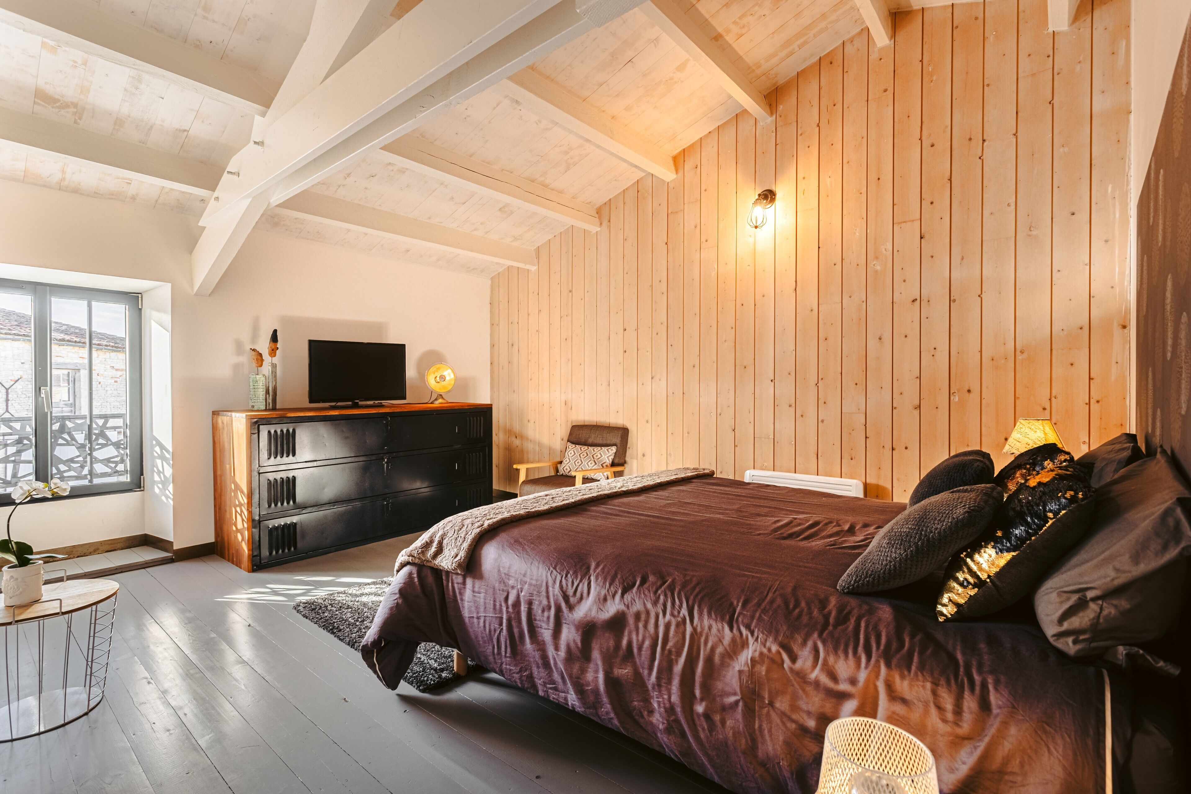 Un dormitorio con una cama grande, paredes de madera, un televisor, un aparador y una silla.