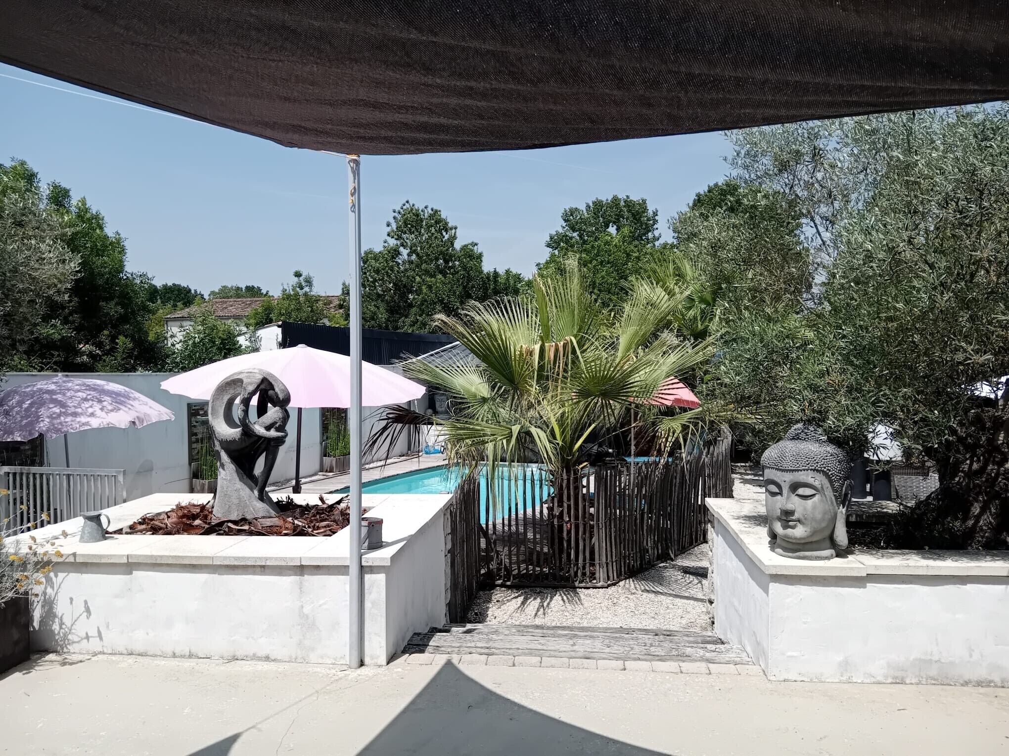 A pool area with a statue, a palm tree, and a shaded umbrella.