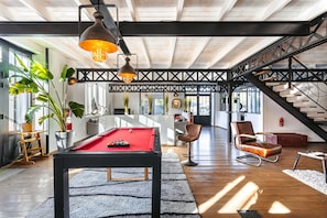 Une pièce spacieuse avec une table de billard, un escalier et une vue sur l’extérieur.