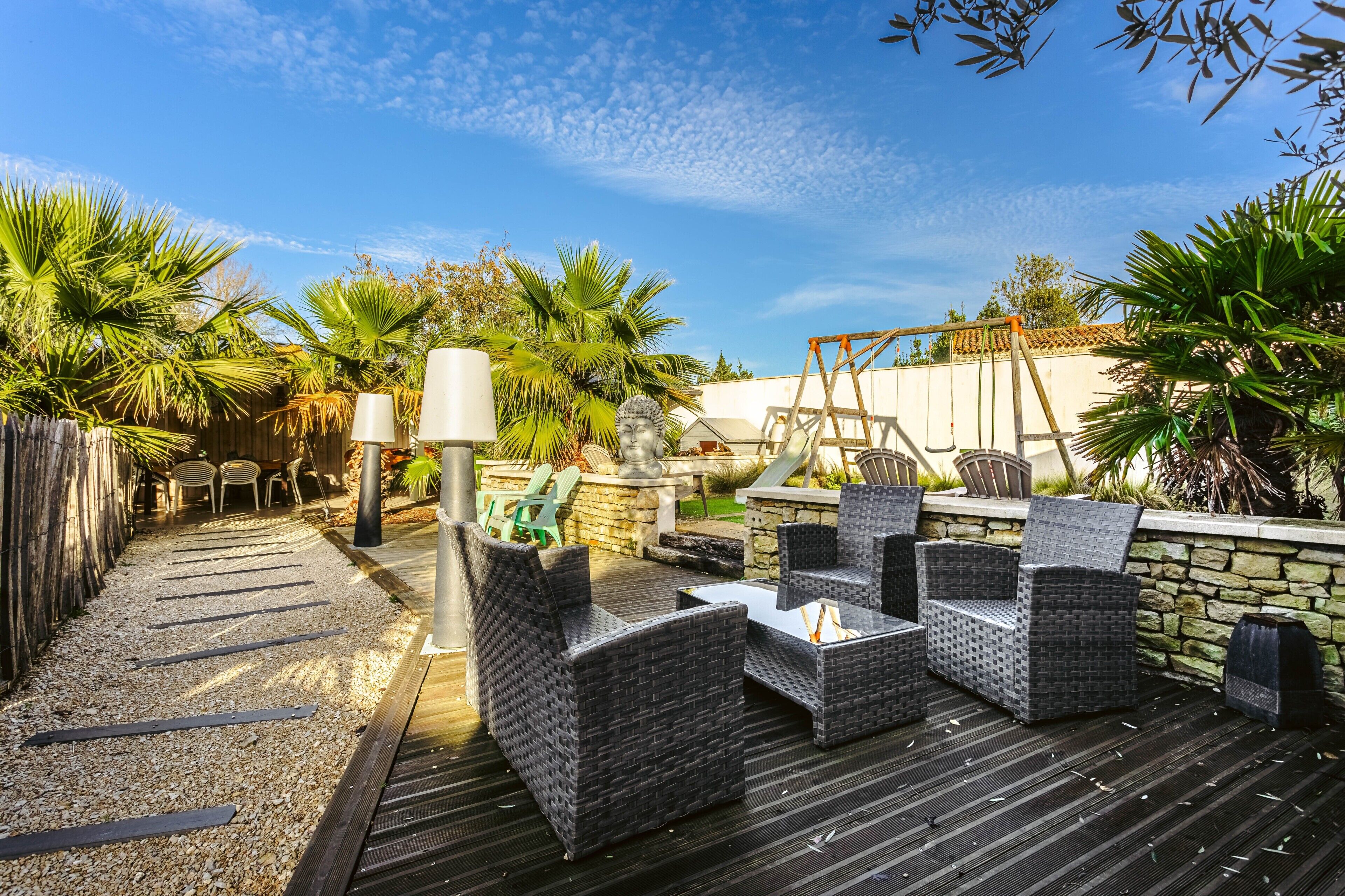 An outdoor patio with wicker furniture, a stone wall, and a swing set.