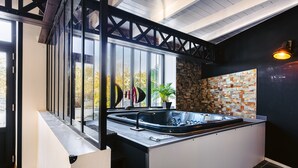 A modern kitchen with a large window, a built-in hot tub, and a stone wall backsplash. - 'Villa la Forge Expérience Bien-Être' with Pool & Wi-Fi (Nuaillé-d'Aunis)