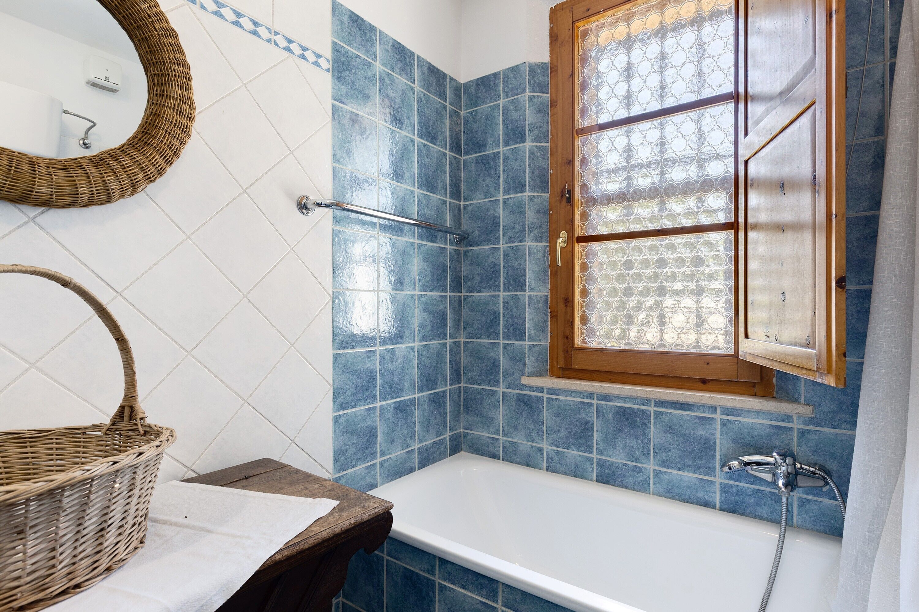 A bathroom with a bathtub, a wooden-framed window, and a wicker basket.