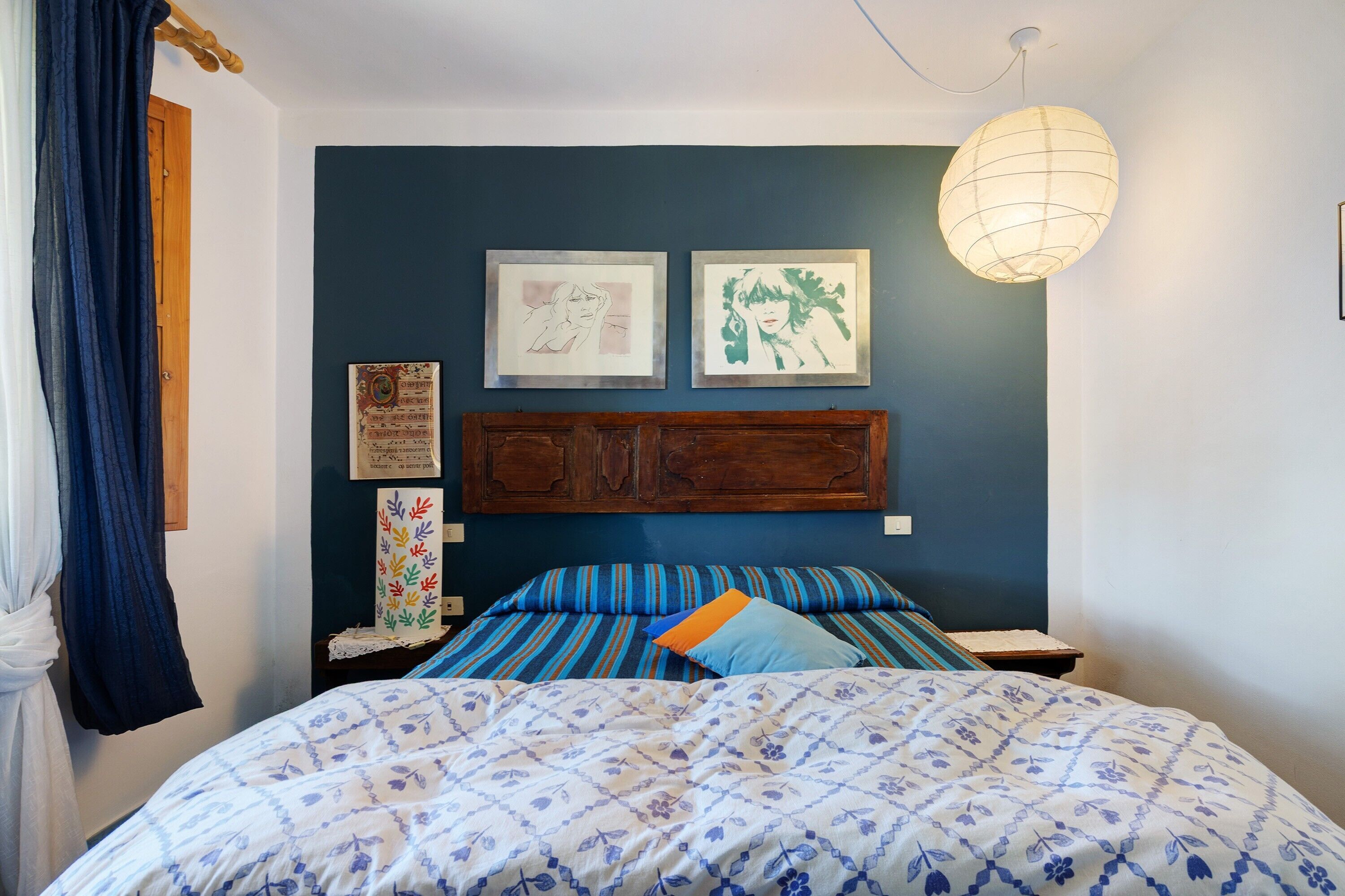 A bedroom with a bed, a headboard, a wall-mounted light, and framed artwork.