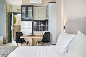 A hotel room with a bed, a desk with two chairs, a kitchenette, and a view of the outside. - Apartment in a Hotel 'Sunset Premium Studio 8' with Sea View, Shared Pool, & Wi-Fi (Lefkada)