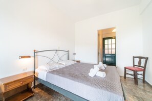 A neatly made bed with a quilted cover, a wooden nightstand with a drawer, a chair with a red cushion, and a door leading to another room. - Studio "Arianna Studio Ground Floor 5" with Sea View, Shared Pool & Wi-Fi (Corfu)