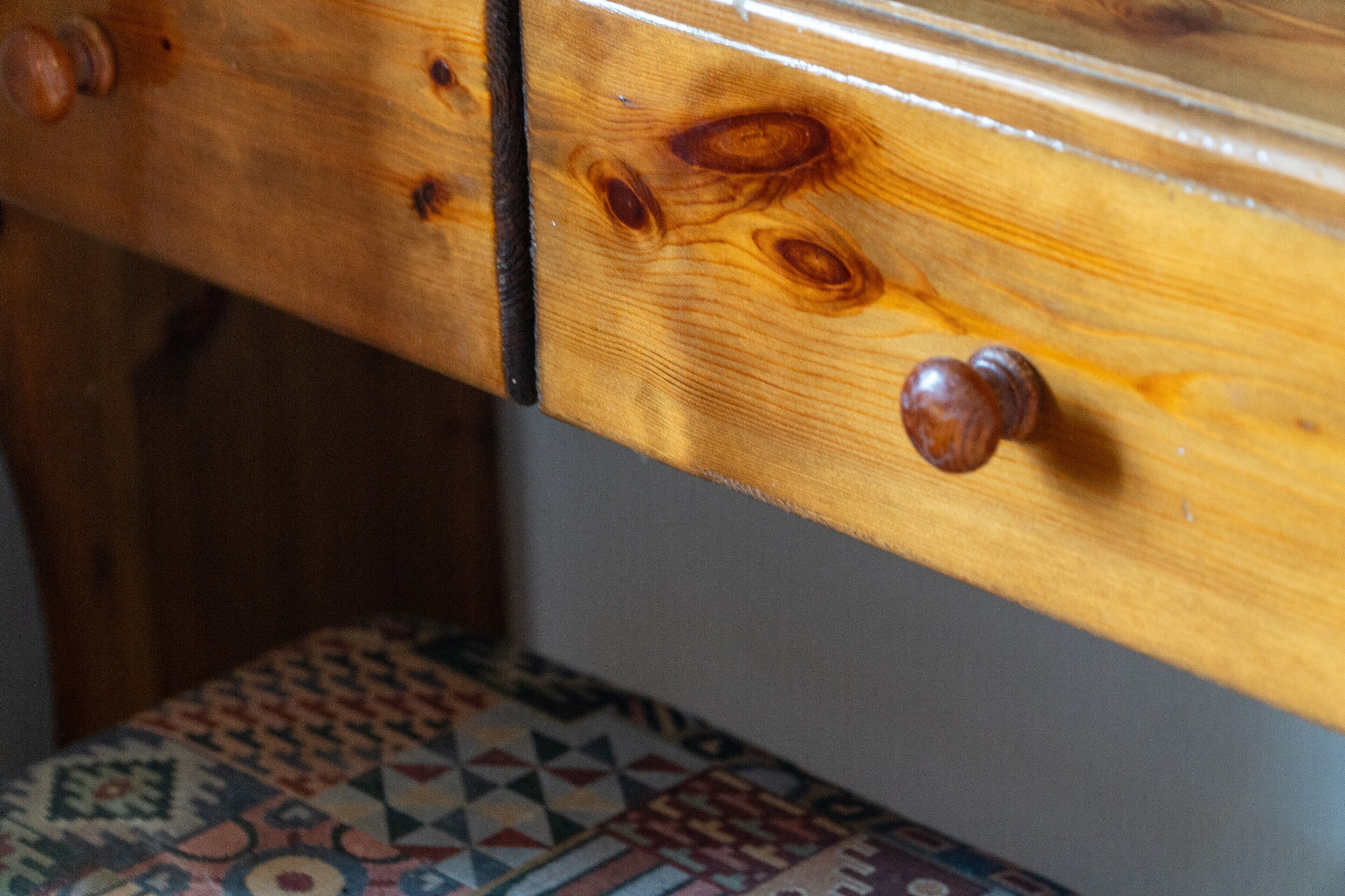 Un tiroir en bois avec un bouton, un coussin à motifs et une surface en bois dont on peut distinguer les veines.