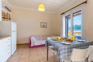 Una habitación con una mesa de comedor para dos personas, una cama, un ventanal con vistas y una pequeña cocina.
