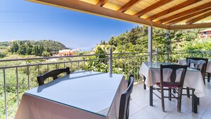 Een terras buiten met tafels en stoelen, een houten pergola en uitzicht op een heuvel.