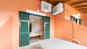 Een kamer met een bed, een tafel en stoelen, met groene luiken en airconditioners.