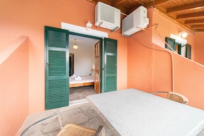 A room with a bed, a table, and chairs, with green shutters and air conditioning units.
